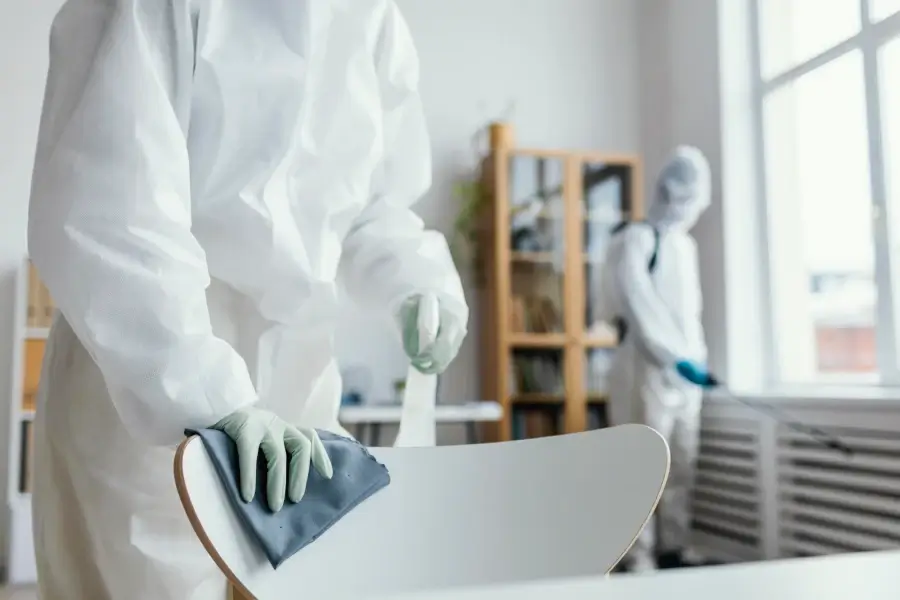 An individual wearing a white protective suit and gloves cleans an office chair as part of a disinfection service in Singapore.